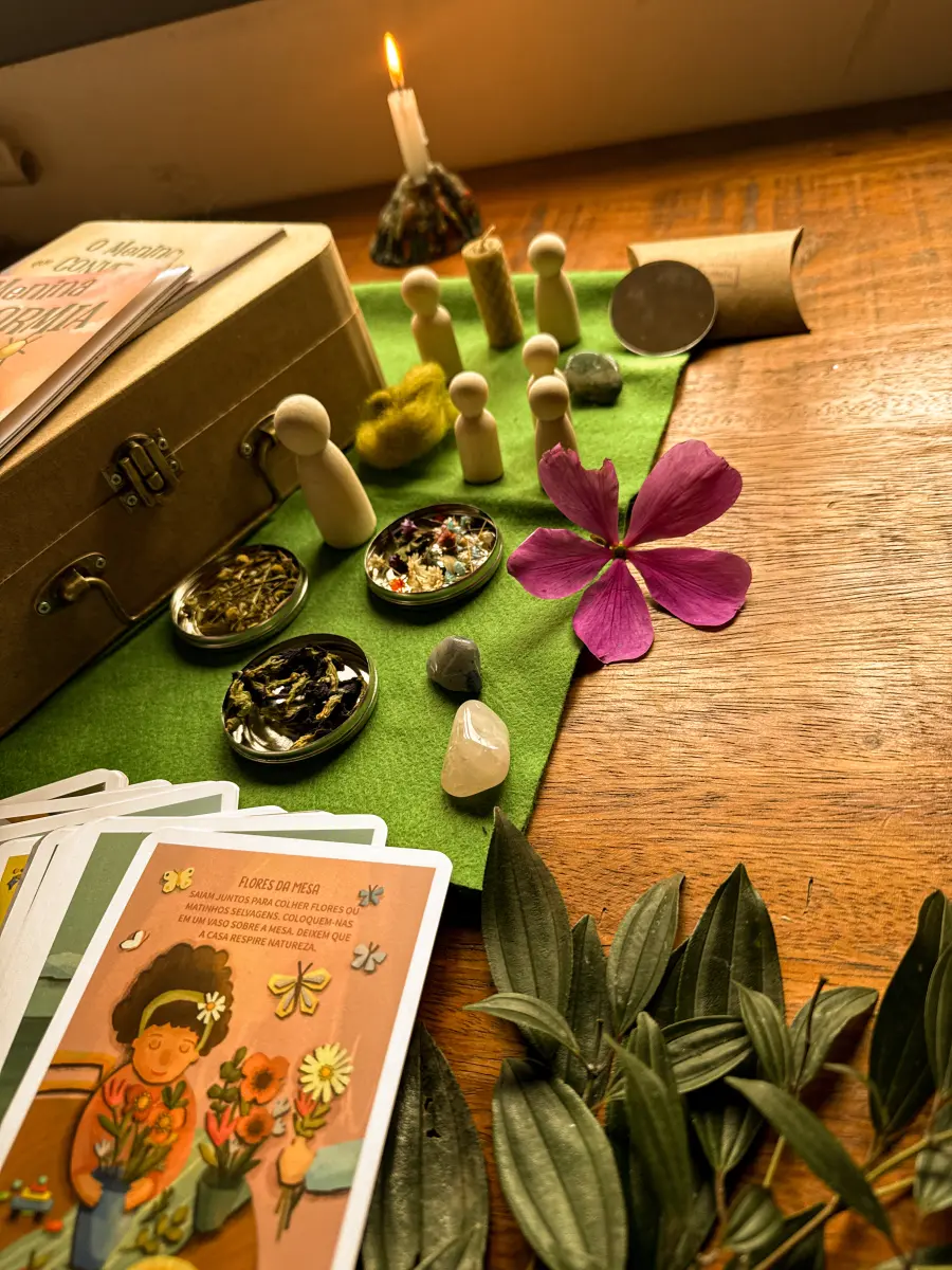 Espaço de Afeto montado sobre a mesa: o feltro verde estendido fora da maleta, com bonequinhos, latinhas de ervas, pedras e cartas do Oráculo dos Afetos ao redor