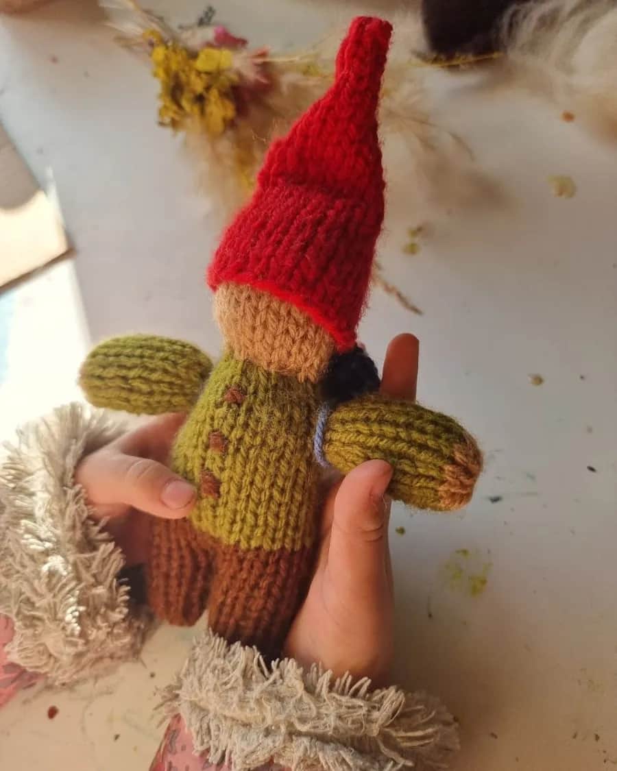 Mãos segurando um gnomo de tricô de gorro vermelho