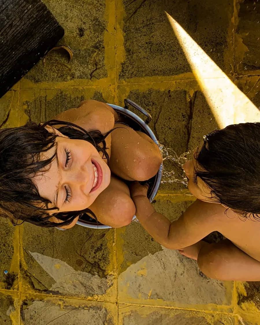 Duas crianças sorrindo ao sol, brincando juntas numa bacia de água