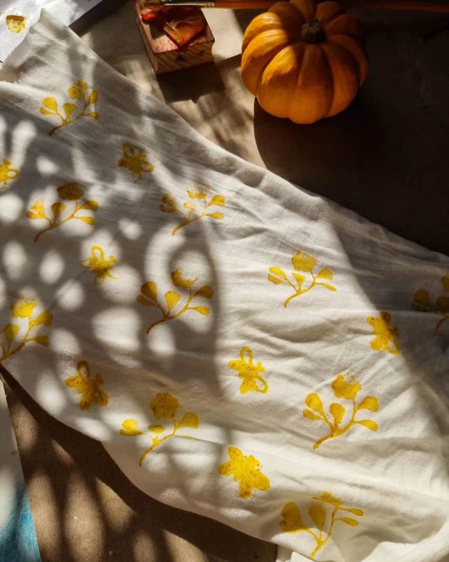 Tecido tingido com flores amarelas estendido ao sol, com uma abóbora ao lado