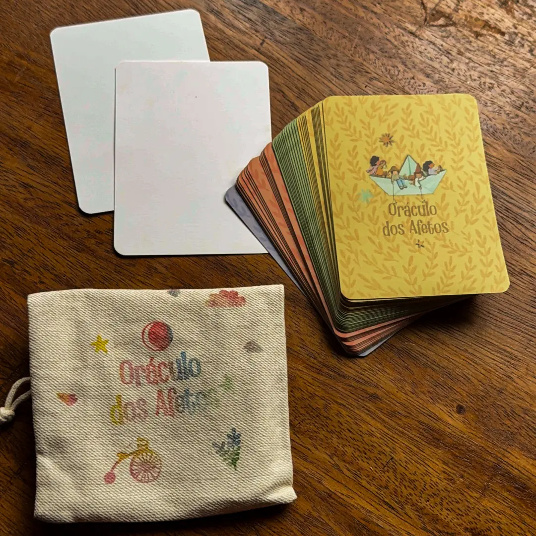 O saquinho de tecido do Oráculo dos Afetos sobre uma mesa de madeira, com duas cartas em branco ao lado e o baralho aberto em leque.